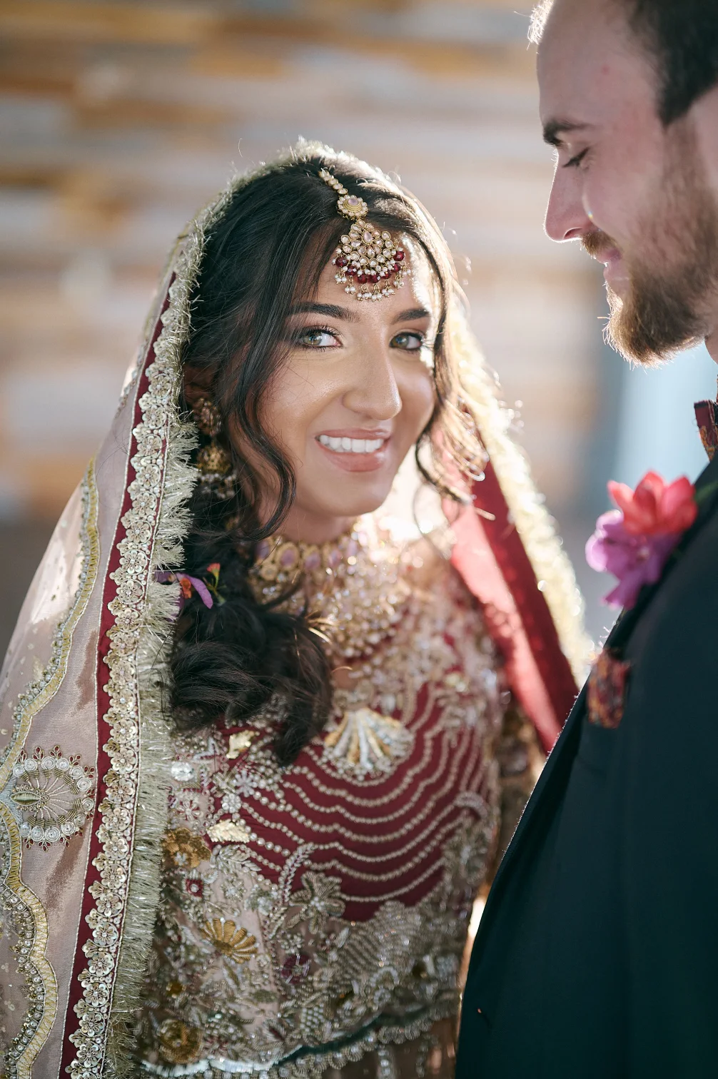 Beautiful Indian bride smiling at camera, while groom looks at her.